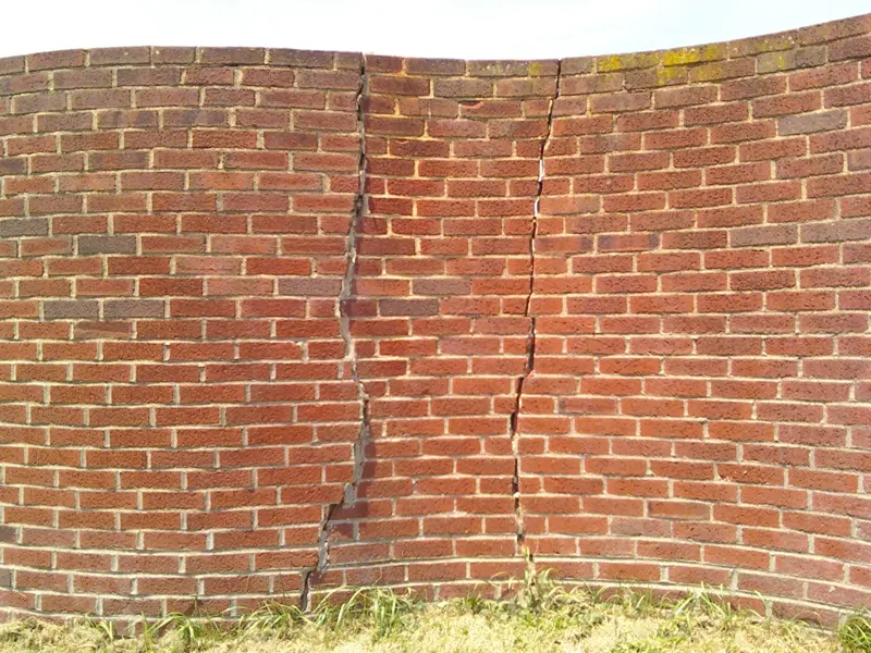 Long brick wall with stair-step cracks running through the mortar joints